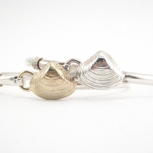May include: Two silver bracelets with a clam shell charm. One charm is gold and the other is silver.