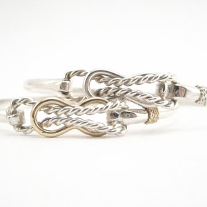 May include: Two silver bracelets with a rope design. The bracelets are linked together with a gold accent.