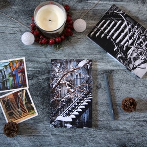 A winter notebook featuring a black and white photograph of Montreal's snow-covered spiral walk-up stairs with parked bicycles covered in snow. The notebook is surrounded by other Montreal notebooks and mini prints that can be framed or sent as cards.

The hand-bound notebooks measure 5x8 inches. They contain 48 pages of cream-white acid free paper with a smooth finish. The matte cover is smooth and scuff-resistant!

Each notebook comes with an insert containing 15 insightful journaling prompts!