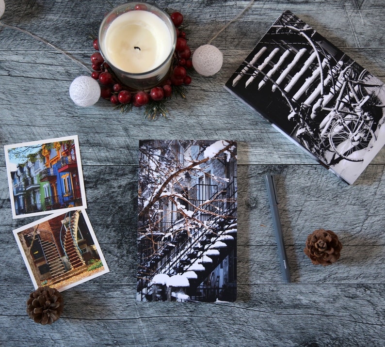 A winter notebook featuring a black and white photograph of Montreal's snow-covered spiral walk-up stairs with parked bicycles covered in snow. The notebook is surrounded by other Montreal notebooks and mini prints that can be framed or sent as cards.

The hand-bound notebooks measure 5x8 inches. They contain 48 pages of cream-white acid free paper with a smooth finish. The matte cover is smooth and scuff-resistant!

Each notebook comes with an insert containing 15 insightful journaling prompts!