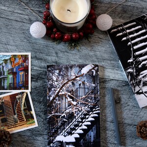 A winter notebook featuring a black and white photograph of Montreal's snow-covered spiral walk-up stairs with parked bicycles covered in snow. The notebook is surrounded by other Montreal notebooks and mini prints that can be framed or sent as cards.

The hand-bound notebooks measure 5x8 inches. They contain 48 pages of cream-white acid free paper with a smooth finish. The matte cover is smooth and scuff-resistant!

Each notebook comes with an insert containing 15 insightful journaling prompts!