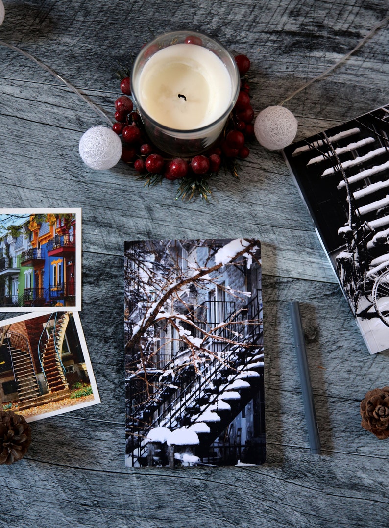 A winter notebook featuring a black and white photograph of Montreal's snow-covered spiral walk-up stairs with parked bicycles covered in snow. The notebook is surrounded by other Montreal notebooks and mini prints that can be framed or sent as cards.

The hand-bound notebooks measure 5x8 inches. They contain 48 pages of cream-white acid free paper with a smooth finish. The matte cover is smooth and scuff-resistant!

Each notebook comes with an insert containing 15 insightful journaling prompts!