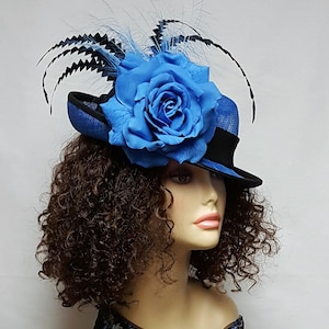 May include: A blue and black hat with a large blue rose and black and blue feathers. The hat has a black brim and a blue woven top. The rose is the focal point, adding a touch of elegance to the design. A stylish accessory for special occasions.