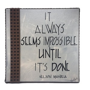 May include: A white canvas with a brown patterned border. The canvas has a black handwritten quote that reads "It always seems impossible until it's done - Nelson Mandela".