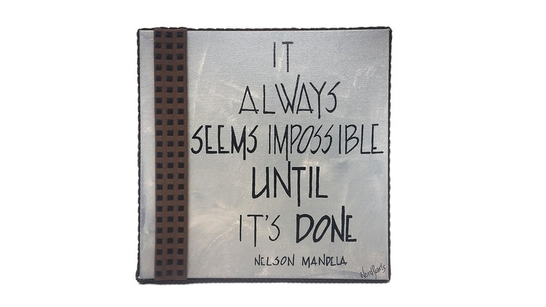 May include: A white canvas with a brown patterned border. The canvas has a black handwritten quote that reads "It always seems impossible until it's done - Nelson Mandela".