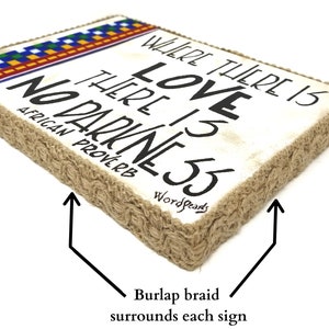 May include: A white wooden sign with the text "Where there is love there is no darkness" in black lettering. The sign is surrounded by a brown burlap braid and has a colorful patterned border at the top. The text "African Proverb" is written below the main text and "Wordsparks" is written below that.