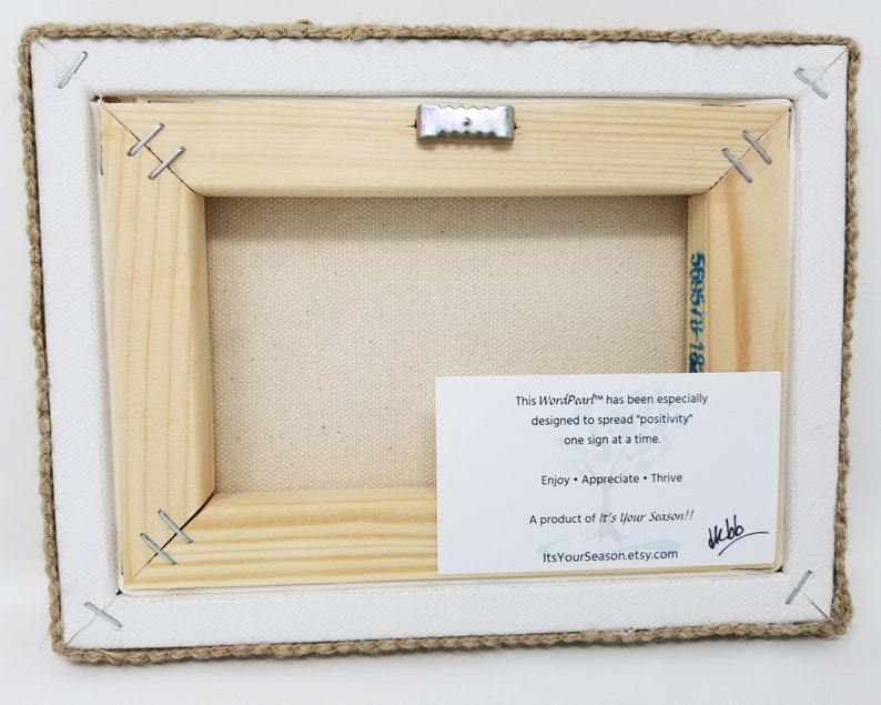 May include: A wooden framed canvas print with a white background and a burlap border. The back of the canvas has a white card with the text "This Won'Port&trade; has been especially designed to spread "positivity" one sign at a time. Enjoy &bull; Appreciate &bull; Thrive A product of It's Your Season!! ItsYourSeason.etsy.com" and a handwritten signature.