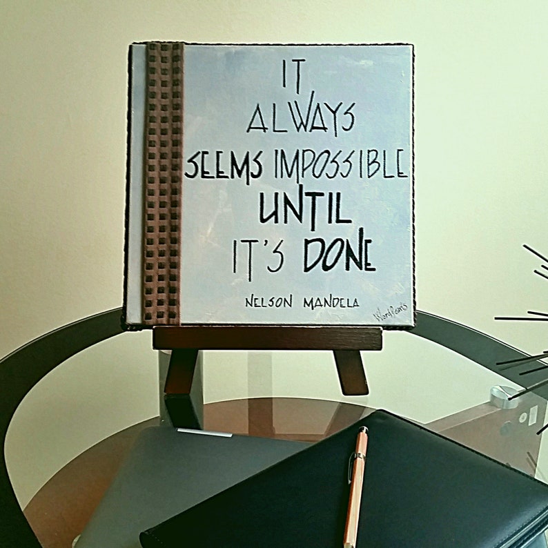 May include: A motivational quote by Nelson Mandela on a blue canvas with a brown patterned border. The quote reads "It always seems impossible until it's done".