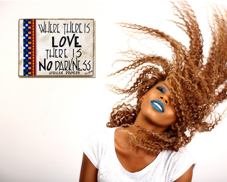 May include: A woman with long, curly, light brown hair is smiling with her head tilted back. She is wearing blue lipstick and blue eyeshadow. The background is white with a sign that reads "Where there is love there is no darkness. African proverb."
