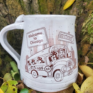 May include: White ceramic mug with a brown illustration of a school bus with the words "Welcome to Chicago", "New Orleans", "Good People On Board", "School's Bus Go" and a peace sign.