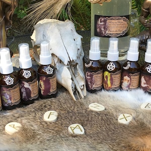 May include: A collection of 14 small glass bottles with brown labels and silver spray tops, arranged in a row on a table. The bottles are filled with a clear liquid. There is a larger glass bottle with a brown label and a silver cap in the center of the image. The bottle is filled with a clear liquid. There is a skull, a fur pelt, and a few wooden runes on the table. The bottles are labeled with the text "Magickal Mist" and "Dance in the Sun".
