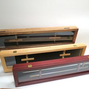 May include: Three wooden display cases with glass fronts for storing swords. The top case is made of dark wood, the middle case is made of light wood, and the bottom case is made of red wood.