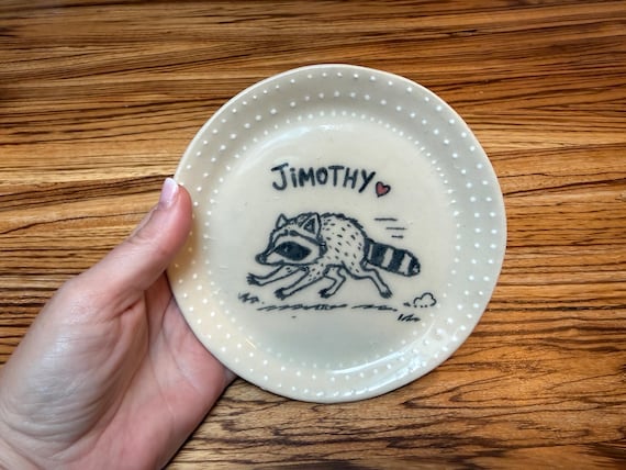 A hand-sculpted ceramic trinket dish featuring Jimothy the Raccoon — specific enough in personality and craft to feel totally one-of-a-kind, not a generic animal print.