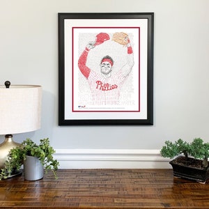 May include: Framed art print featuring a baseball player in a Phillies uniform, holding a cap and glove. The image is composed of text, with the Phillies logo and player's name visible. The frame is black, and the print has a red border.