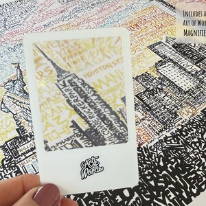 May include: A detailed map print featuring a cityscape with the Empire State Building highlighted within a white frame. The map is filled with text and includes a magnifying glass with the text "Includes an Art of Words Magnifier!"