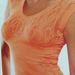 May include: A sleeveless, peach-colored top with a delicate lace pattern. The top has a scoop neckline and a fitted silhouette.