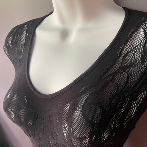 May include: Black lace top with a scoop neck and short sleeves. The lace pattern is floral and has a mesh design.