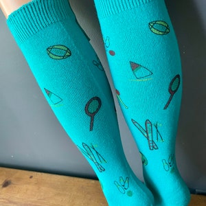 May include: A pair of turquoise knee-high socks with a pattern of various sports equipment, including tennis rackets, skis, bowling pins, and a ball.