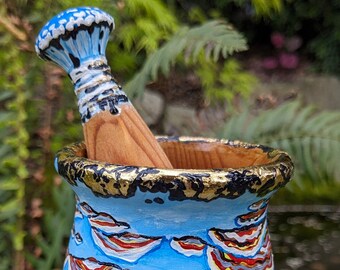 May include: A blue and white ceramic mortar and pestle with a wooden pestle. The mortar is decorated with a swirling pattern of red, yellow, and white lines. The pestle has a blue and white top.