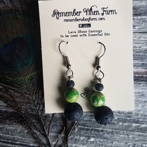 May include: A pair of lava stone earrings with green and black beads. The earrings are on a white card with the text "Remember When Farm" and "Lava Stone Earrings to be used with Essential Oils".
