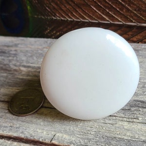 May include: A white, round, ceramic knob with a smooth surface. The knob is slightly textured and has a subtle sheen.
