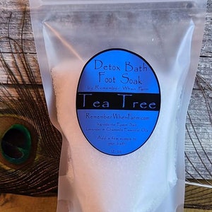 May include: A white plastic bag with a blue label that reads "Detox Bath Foot Soak by Remember When Farm Tea Tree". The label also includes the website "RememberWhenFarm.com", ingredients, and instructions for use. The bag contains a white powder and is 12 oz.