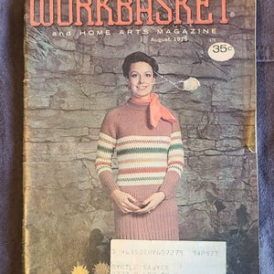 May include: Vintage August 1975 issue of "The Workbasket" magazine. The cover features a woman in a pink knit sweater and skirt with a striped design. The magazine cover has a price of 35 cents.