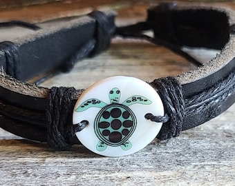 May include: Black leather bracelet with a white turtle charm. The turtle has a green shell and black markings.