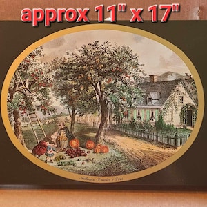 May include: A framed oval print of a vintage illustration depicting a farmhouse with a tree full of apples. The scene includes a family picking apples and the text "Autumn Candies & Trees". The frame is black with a gold inner border. The print measures approximately 11 inches by 17 inches.