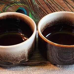 May include: Two brown and white ceramic mugs with a glazed finish. The mugs have a rounded shape and a handle on the side.