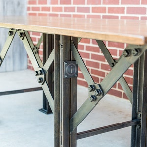 May include: A wooden table with a metal base. The base is made of black metal and has a criss-cross pattern. The table is supported by four legs.