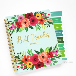 May include: A teal blue bill tracker journal with a floral design featuring pink, red, yellow, and green flowers. The journal has a gold spiral binding and a tabbed section for each month of the year.