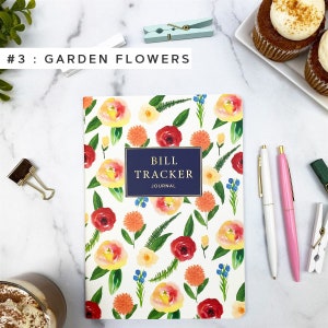 Puede incluir: Un cuaderno blanco con un patr&oacute;n floral con flores rojas, naranjas, amarillas y azules. El cuaderno tiene un t&iacute;tulo azul marino que dice "Bill Tracker Journal".