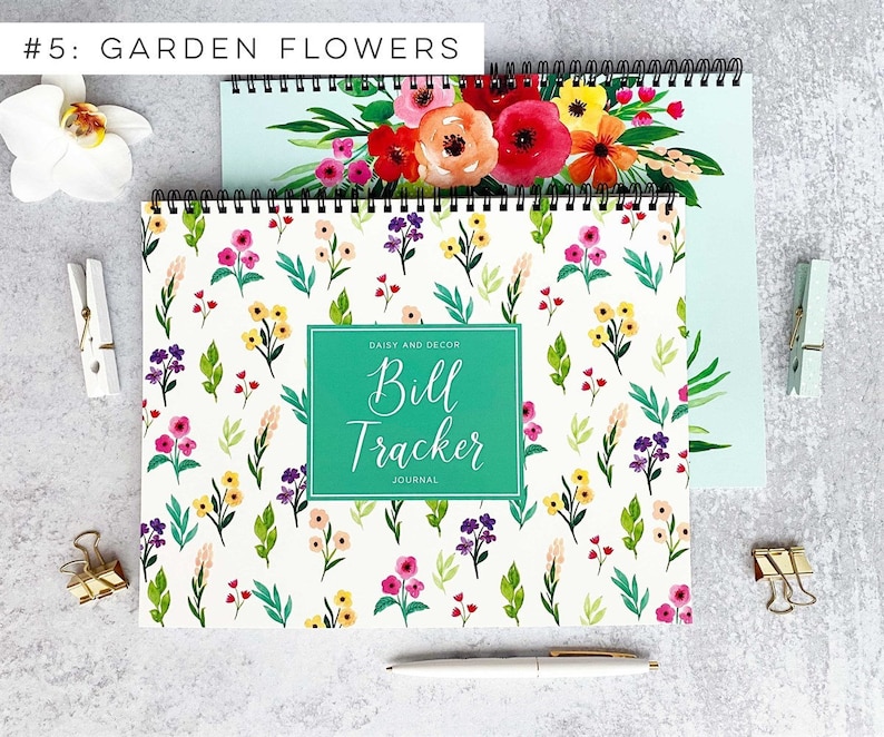 May include: A white spiral bound journal with a teal green cover that says "Daisy and Decor Bill Tracker Journal". The cover has a floral pattern with pink, yellow, and purple flowers on a white background.