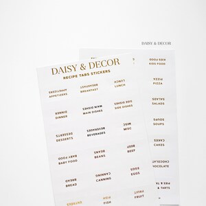 May include: A set of white recipe tabs with gold lettering. The tabs are labeled with different food categories, such as appetizers, breakfast, lunch, dinner, desserts, beverages, main dishes, side dishes, soups, salads, and more. The tabs are designed to help organize recipes in a binder or cookbook.