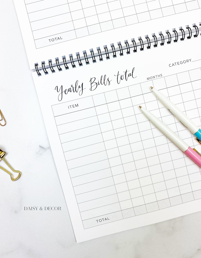 K&ouml;nnte beinhalten: Ein wei&szlig;er Spiralplaner, der auf einer Seite "Yearly Bills total" ge&ouml;ffnet ist. Die Seite hat ein Rasterlayout f&uuml;r detaillierte Ausgaben. Zwei Stifte mit wei&szlig;en Sch&auml;ften und goldenen Spitzen, einer mit rosa Ende und der andere mit blauem Ende, liegen auf der Seite.
