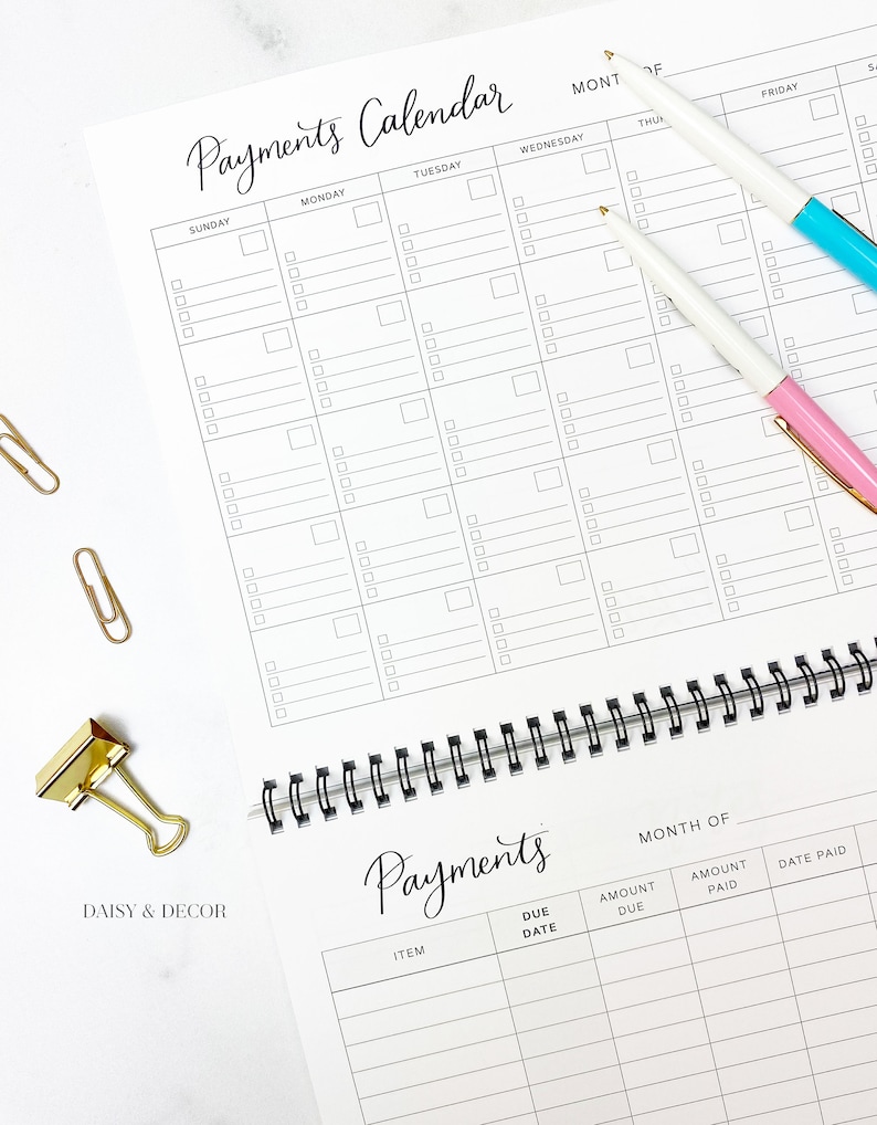 K&ouml;nnte beinhalten: Ein wei&szlig;er, spiralgebundener Zahlungskalender mit schwarzem Raster. Der Kalender enth&auml;lt den Text "Payments Calendar" in eleganter Schrift. Zwei Stifte, einer mit rosa und einer mit blauem Akzent, sowie goldene B&uuml;roklammern sind ebenfalls sichtbar.
