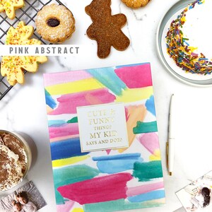 Puede incluir: Un diario de acuarela rosa, azul y amarillo con el texto "Cute & Funny Things My Kid Says and Does" y "Daisy & Decor" en la portada. El diario est&aacute; rodeado de galletas, un pastel y fotos.