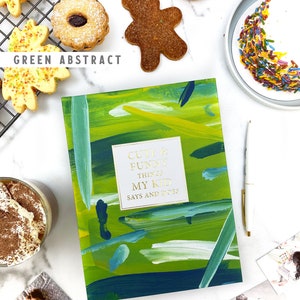 Puede incluir: Un diario verde con pinceladas abstractas y el texto "Cute & Funny Things My Kid Says and Does" en la portada. El diario est&aacute; abierto para revelar una p&aacute;gina en blanco. El diario est&aacute; rodeado de varios art&iacute;culos, que incluyen galletas, un cupcake, una taza de caf&eacute; y fotos.