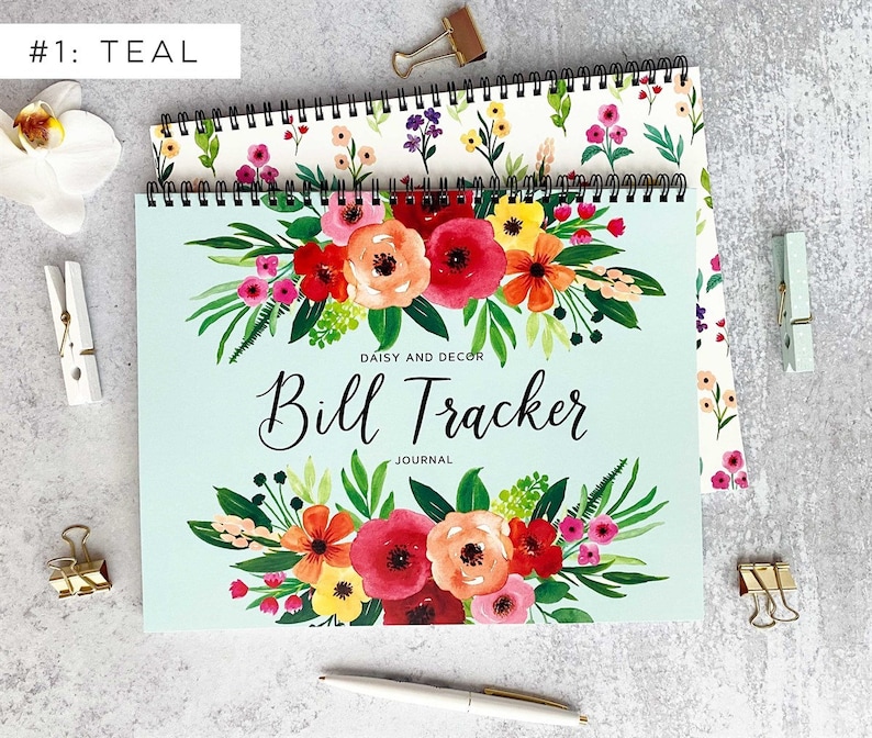 May include: Teal blue spiral bound journal with a floral design featuring red, orange, yellow, and pink flowers. The journal cover has the text "Daisy and Decor Bill Tracker Journal".