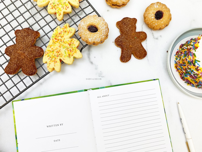 Puede incluir: Un cuaderno con una cubierta verde y las palabras "All About" escritas en la p&aacute;gina derecha. La p&aacute;gina izquierda tiene las palabras "Written By" y "Date" escritas en ella. Hay galletas en una rejilla de enfriamiento y un plato de chispas en el fondo.