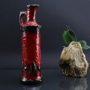 Könnte beinhalten: Eine rote Keramikvase mit schwarzer Glasur und einer strukturierten Oberfläche. Die Vase hat einen Henkel und einen abgerundeten Boden.