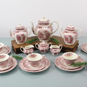 Puede incluir: Un juego de té vintage completo con un diseño floral rojo y blanco. El juego incluye tazas de té, platillos, platos, teteras, azucareras y cremeras. El juego de té está dispuesto sobre una superficie azul claro.