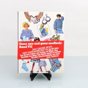 Puede incluir: Un libro rojo y blanco titulado "Ganz neu und ganz modisch: Band VII" con un subtítulo "DAS GROSSE BUCH DER HANDARBEITEN VII" y el texto "Über 100 neue Pullover zum Stricken und Häkeln. Neue Vorschläge zum Nähen. Viele Modelle speziell für Anfänger. Mit vielen Schnittmusterbogen. Extra-Strickkurs."