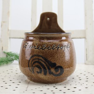 May include: A brown ceramic wall-mounted container with a black swirl design and the text "Zwiebelsuppe" written on the front.