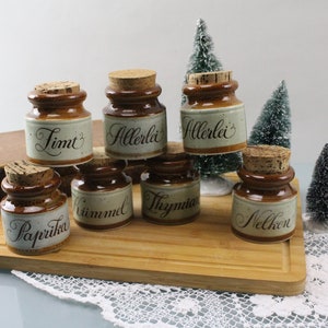 Puede incluir: Conjunto de siete tarros de especias de cerámica marrón con tapas de corcho. Cada tarro tiene una etiqueta de especias diferente en escritura negra: Paprika, Zimt, Allerlei, Nelken, Thymian, Allerlei y Paprika.