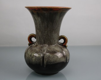Könnte beinhalten: Eine graue Keramikvase mit zwei Henkeln und brauner Glasur. Die Vase hat eine breite Öffnung und einen runden Körper.