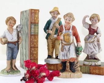 Puede incluir: Conjunto de cinco figuritas de porcelana que representan a personas con ropa tradicional. Las figuritas están pintadas en varios colores, incluyendo rojo, azul, verde y blanco. Las figuritas están de pie sobre pequeñas bases y están dispuestas en una fila.