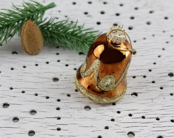 May include: A gold and brown glass bell ornament with a gold glitter design. The ornament has a gold string loop for hanging.