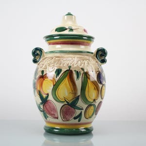 Könnte beinhalten: Ein Keramiktopf mit Deckel, verziert mit handgemalten Obstillustrationen. Der Topf ist cremefarben mit grünen, gelben, roten und violetten Akzenten. Das Wort "Roomtop" ist auf dem Topf geschrieben.
